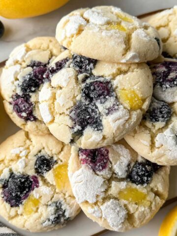 Overhead shot of homemade lemon blueberry cookies on a white kitchen counter with lemons and blueberries scattered around.