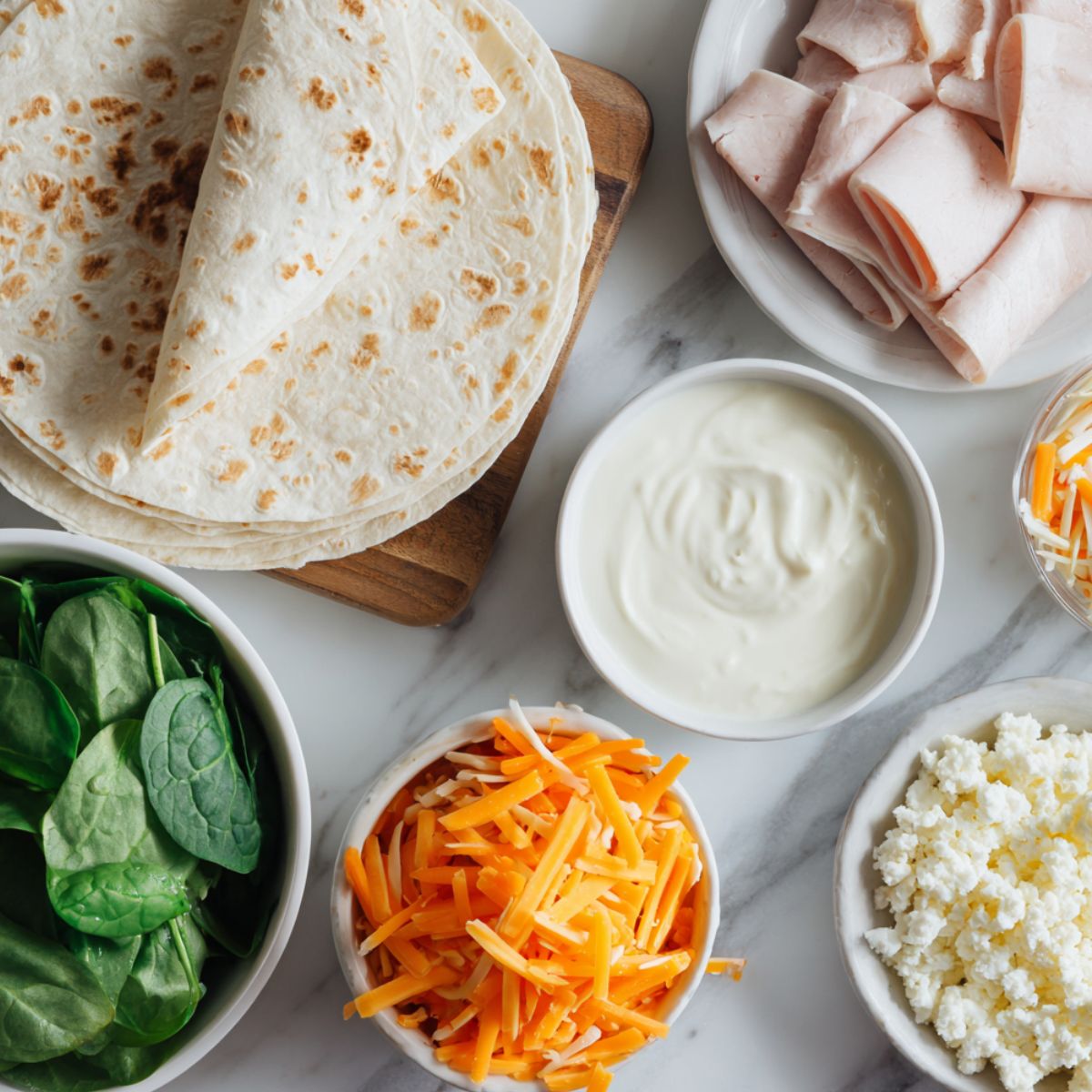 Ingredients for homemade turkey and cheese pinwheel sandwiches arranged casually on a white kitchen counter