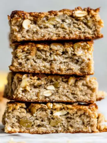 Homemade baked oatmeal breakfast bars on a white kitchen counter, stacked casually with crumbs.
