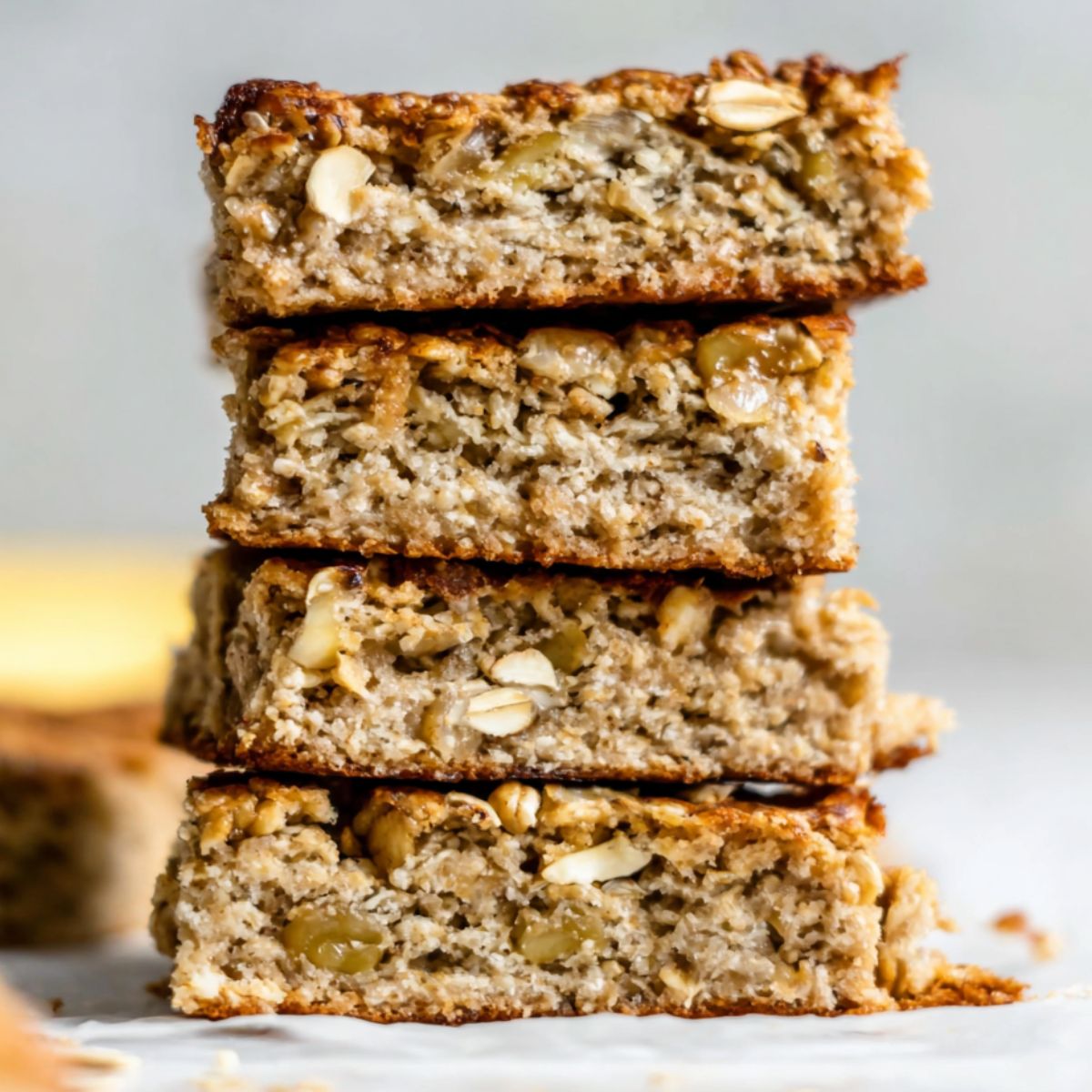 Homemade baked oatmeal breakfast bars on a white kitchen counter, stacked casually with crumbs.