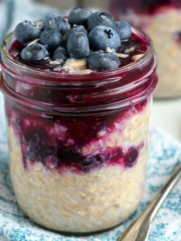 Homemade Blueberry Pie Overnight Oats in a mason jar topped with blueberries and granola on a white kitchen counter.