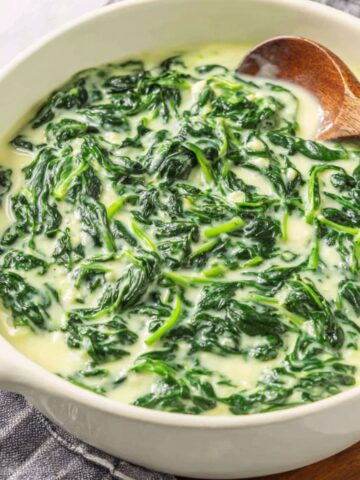 Homemade 3 Ingredient Creamed Spinach​ served in a simple white bowl on a kitchen counter, shot from above.