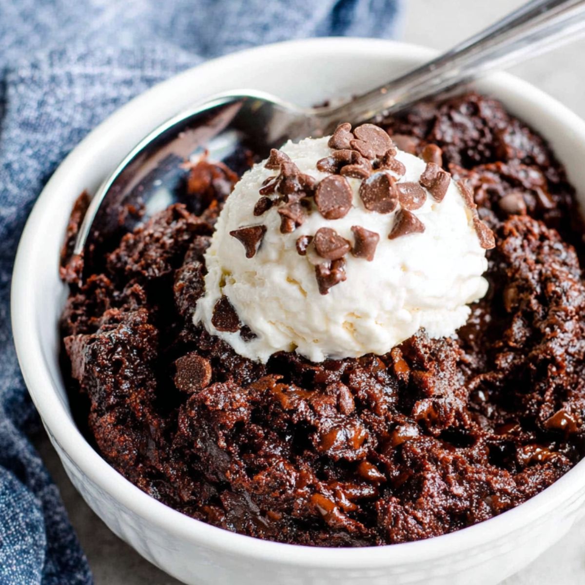 Bowl of homemade edible brownie batter on a white kitchen counter, top-down shot with a spoon inside.