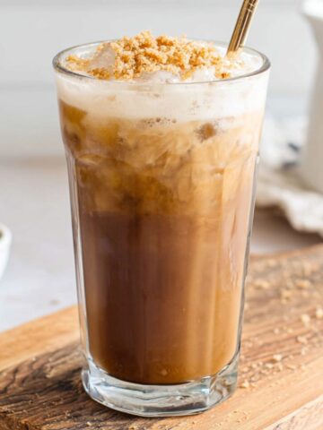 Overhead view of a homemade brown sugar iced coffee with milk swirls and melting ice on a white kitchen counter.