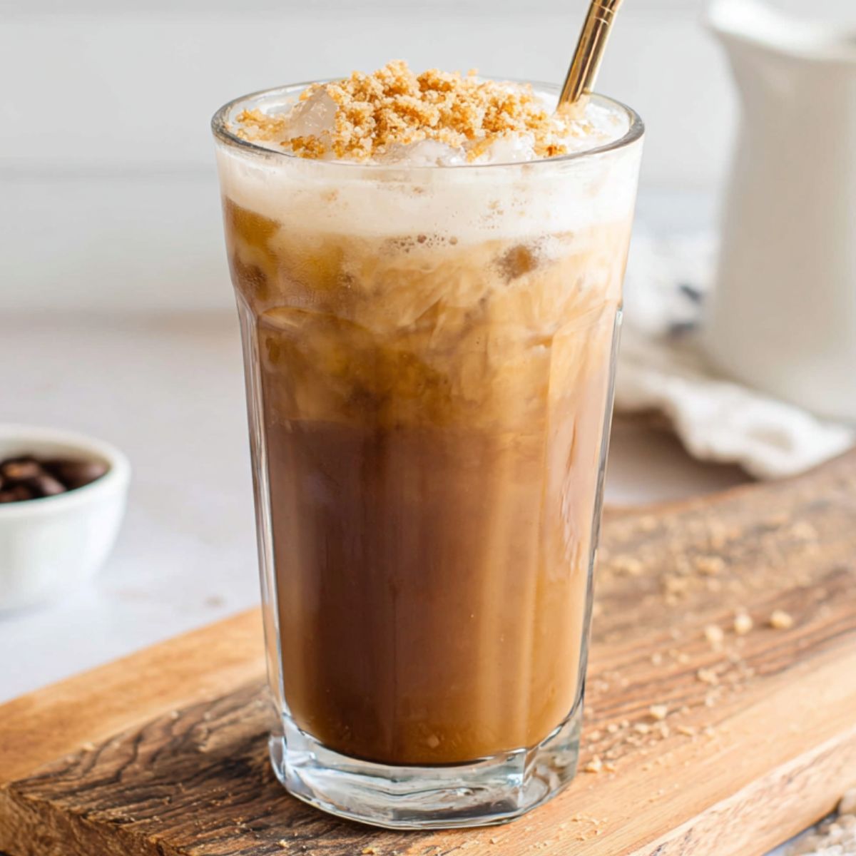 Overhead view of a homemade brown sugar iced coffee with milk swirls and melting ice on a white kitchen counter.