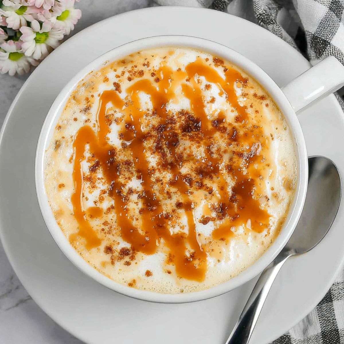 Homemade caramel brulée latte in a ceramic mug on a white kitchen counter, topped with whipped cream and caramel drizzle.