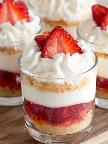 Homemade strawberry cheesecake cups on a white kitchen counter, topped with whipped cream and strawberries,