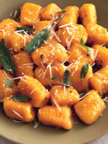 A homemade plate of Sweet Potato Gnocchi Recipe with sage butter sauce on a white kitchen counter.