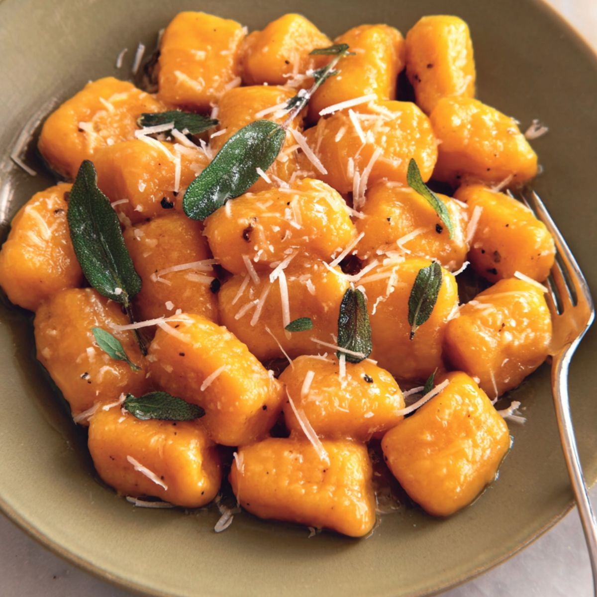 A homemade plate of Sweet Potato Gnocchi Recipe with sage butter sauce on a white kitchen counter.