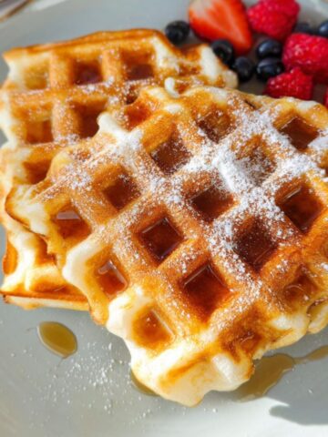 Stack of golden homemade Greek yogurt waffles with berries and honey on a kitchen counter.