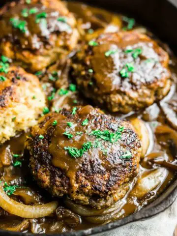 Homemade Amish hamburger steak bake in a glass baking dish with melted cheddar cheese and creamy gravy on a white kitchen counter.