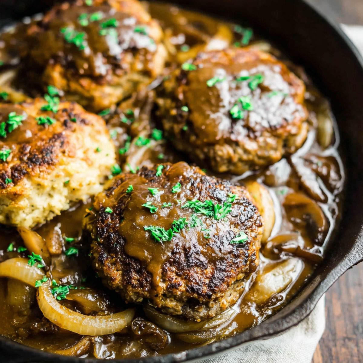 Homemade Amish hamburger steak bake in a glass baking dish with melted cheddar cheese and creamy gravy on a white kitchen counter.
