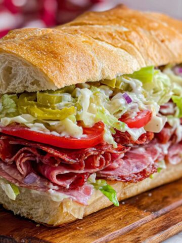 Italian grinder salad sandwich on a wooden cutting board, overflowing with meats, lettuce, tomatoes, and dressing