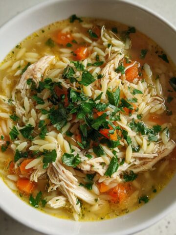 Overhead view of a homemade Italian penicillin soup with chicken on a white kitchen counter.