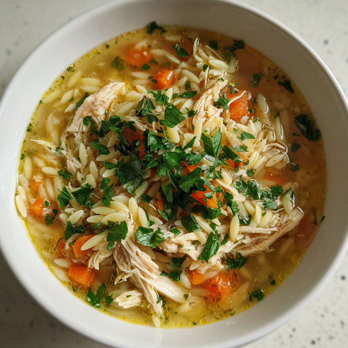 Overhead view of a homemade Italian penicillin soup with chicken on a white kitchen counter.