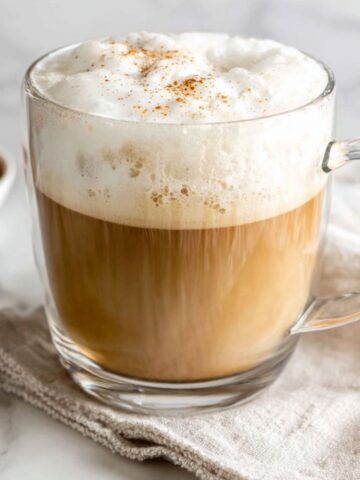Homemade almond milk latte in a glass mug on a white kitchen counter,