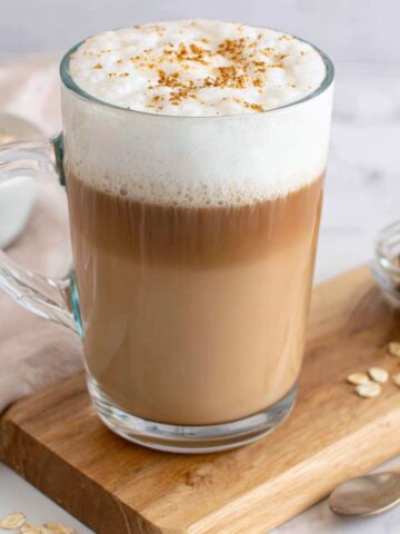 Homemade oat milk latte in a ceramic mug on a white kitchen counter, top-down view.