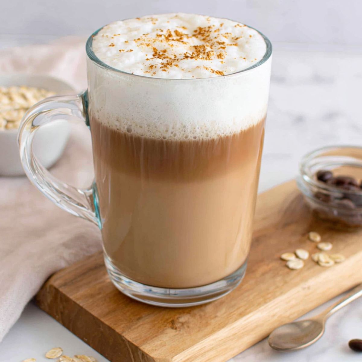Homemade oat milk latte in a ceramic mug on a white kitchen counter, top-down view.