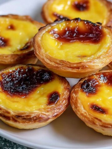 Homemade Portuguese custard tarts on a white kitchen counter with crumbs and golden tops.