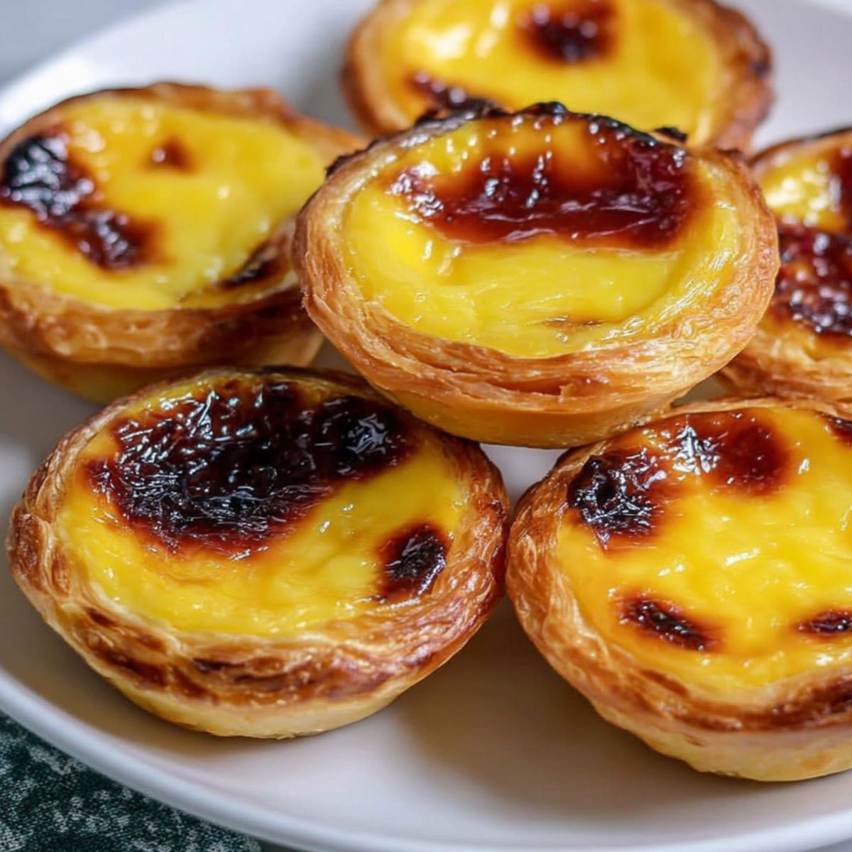 Homemade Portuguese custard tarts on a white kitchen counter with crumbs and golden tops.