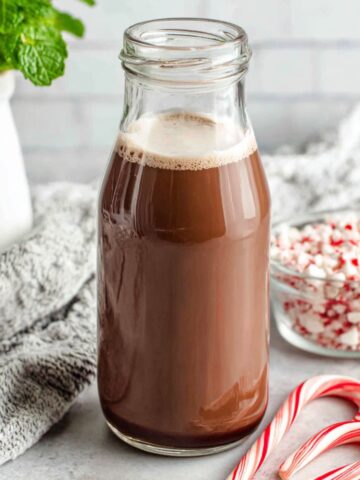 Homemade peppermint mocha creamer in a jar on a white kitchen counter with cocoa and candy canes scattered around.
