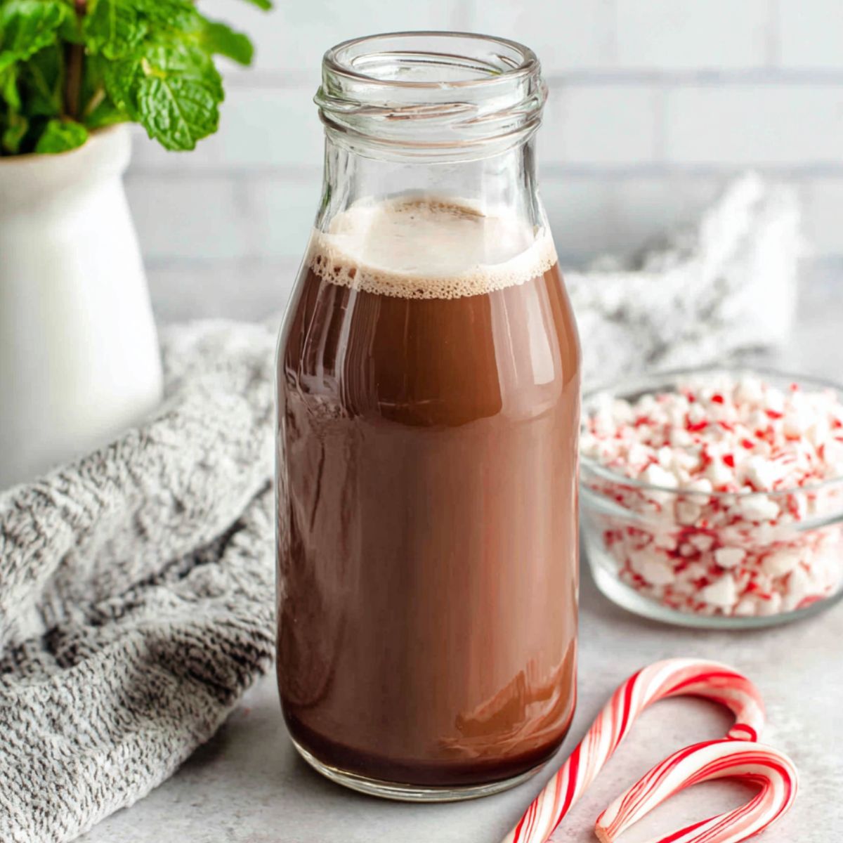 Homemade peppermint mocha creamer in a jar on a white kitchen counter with cocoa and candy canes scattered around.