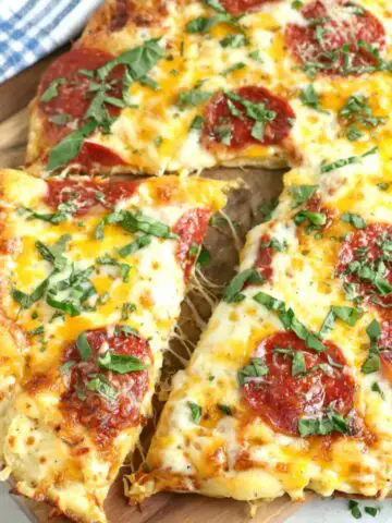 Homemade pizza egg topped with cheese, pepperoni, and basil on a white kitchen counter, top-down view.