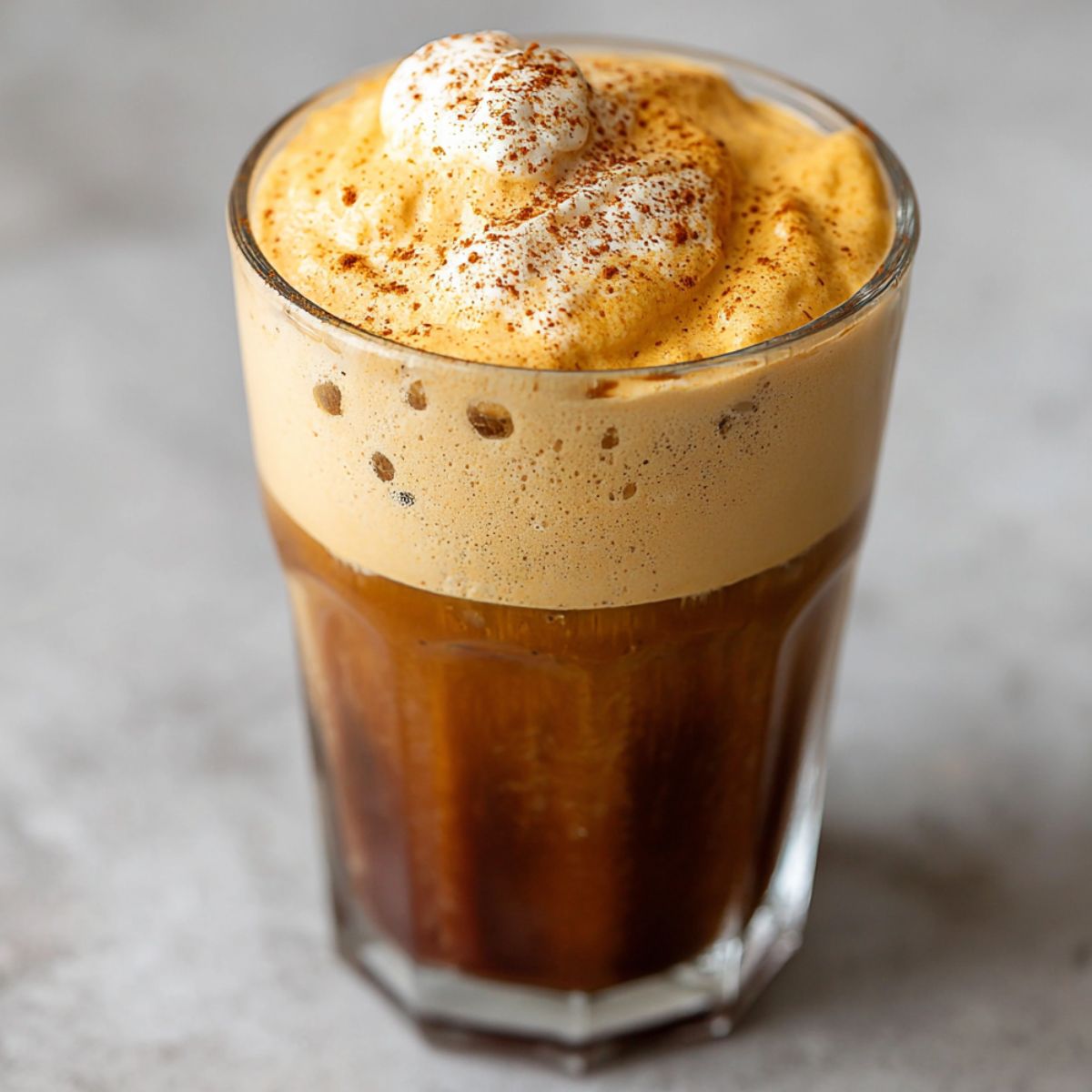 Homemade pumpkin cream cold foam coffee in a clear glass, topped with pumpkin foam and cinnamon on a kitchen counter.