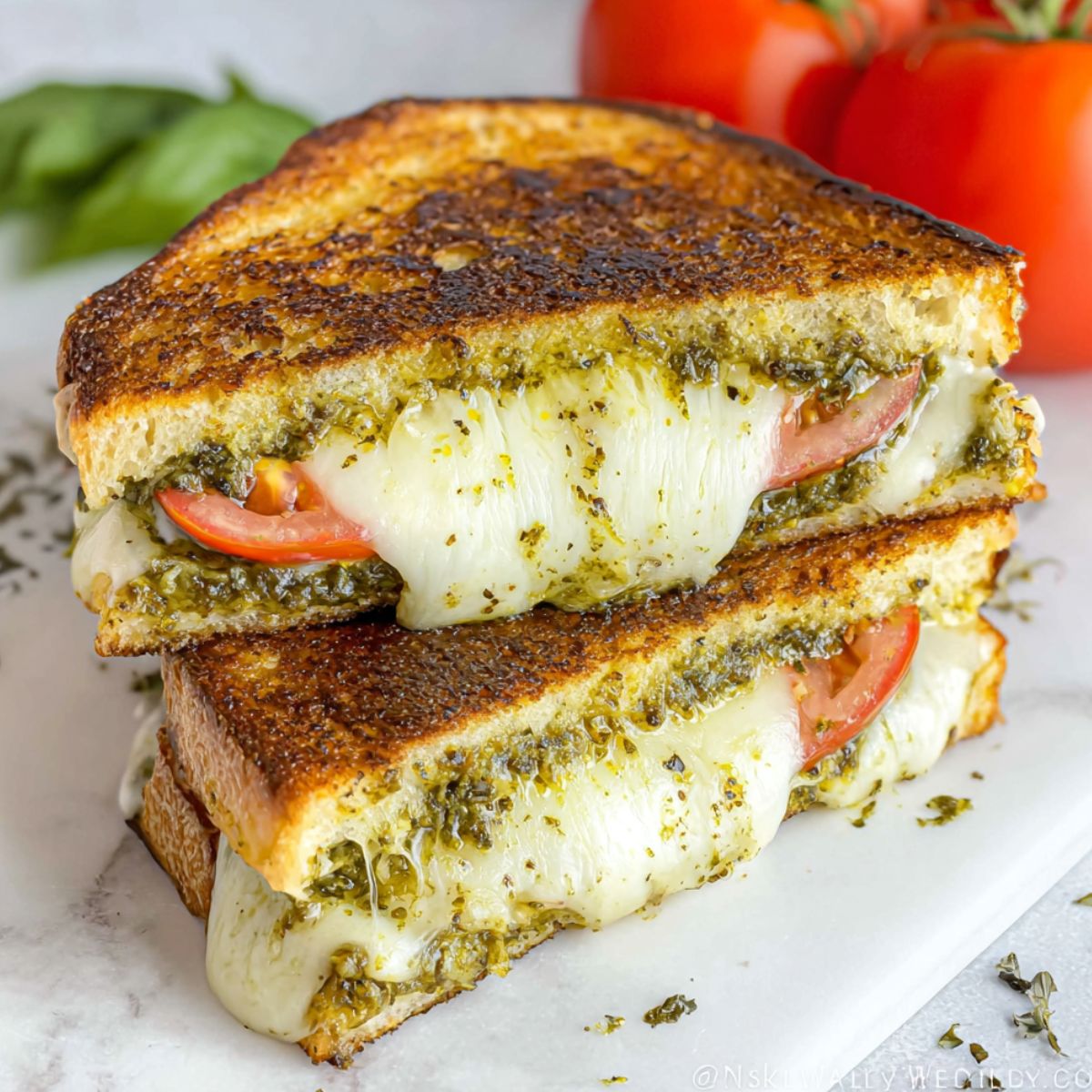 Homemade pesto grilled cheese sandwich on a white kitchen counter, shot from above with melted cheese oozing out.