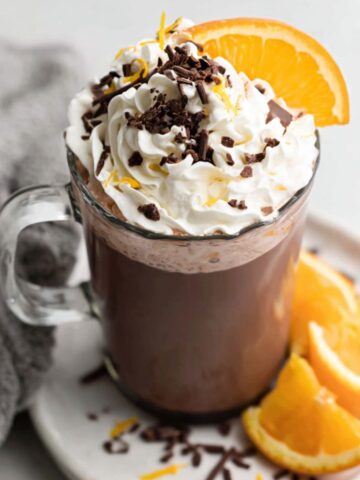 Overhead shot of a homemade orange hot chocolate with whipped cream and orange zest on a white kitchen counter.