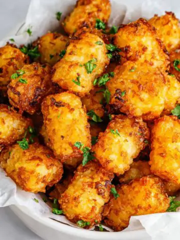 Golden crispy Frozen Tater Tots in Air Fryer basket on a white kitchen counter, overhead shot.