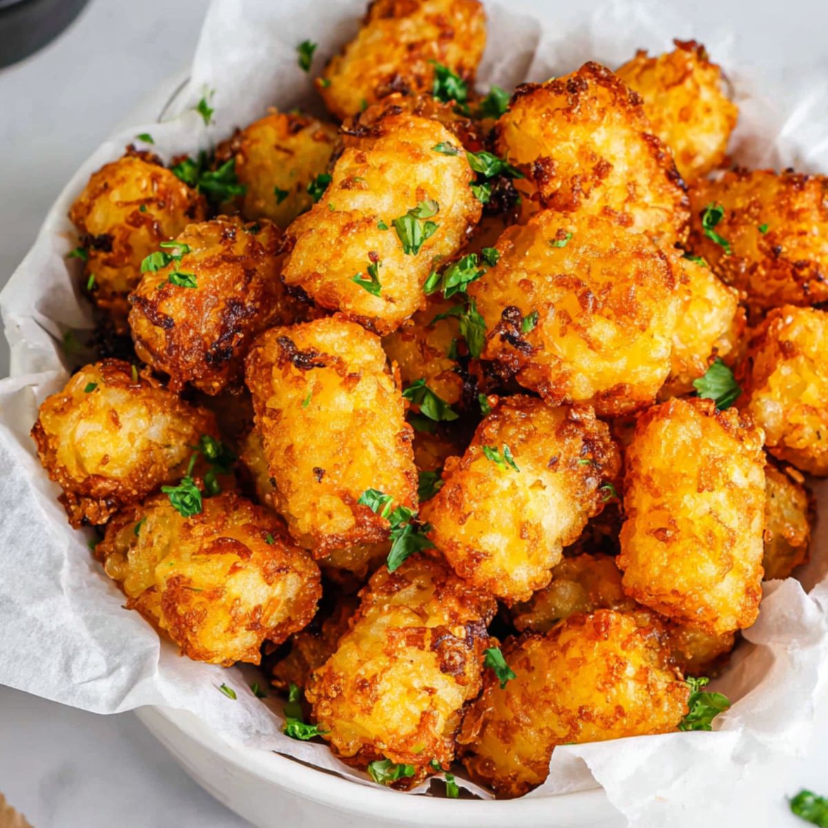 Golden crispy Frozen Tater Tots in Air Fryer basket on a white kitchen counter, overhead shot.