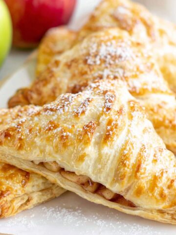Homemade puff pastry apple turnovers cooling on a white kitchen counter, golden and flaky with a rustic homemade look.