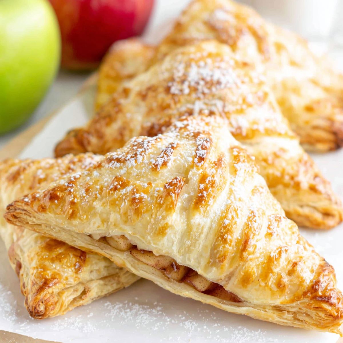 Homemade puff pastry apple turnovers cooling on a white kitchen counter, golden and flaky with a rustic homemade look.