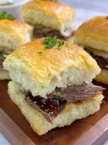 Homemade 3-ingredient slow cooker French dip sandwiches on a white kitchen counter, served with au jus for dipping.
