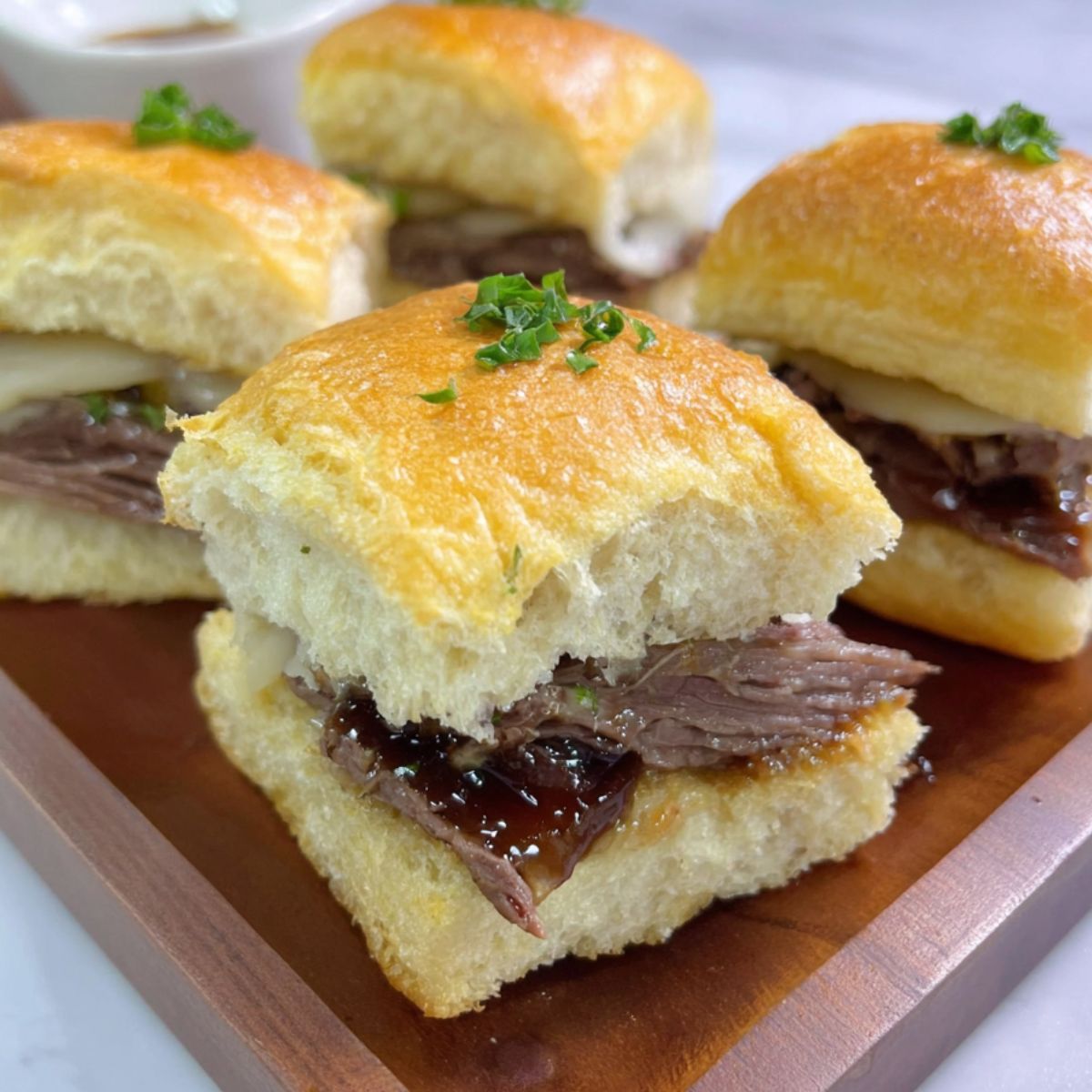 Homemade 3-ingredient slow cooker French dip sandwiches on a white kitchen counter, served with au jus for dipping.