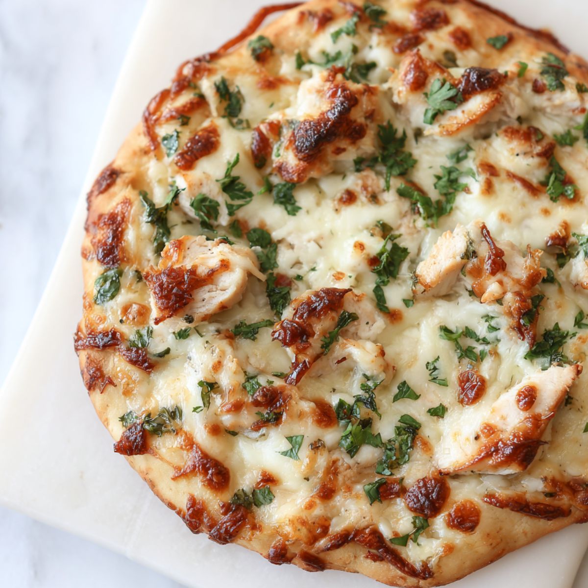 Homemade chicken alfredo flatbread on a white counter