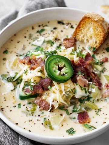 A homemade bowl of jalapeño popper soup with bacon and cheese on a white kitchen counter