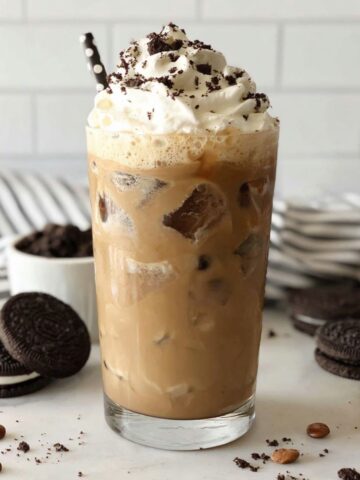 Top-down shot of a homemade Oreo Iced Coffee on a white kitchen counter with whipped cream and cookie crumbs scattered around.