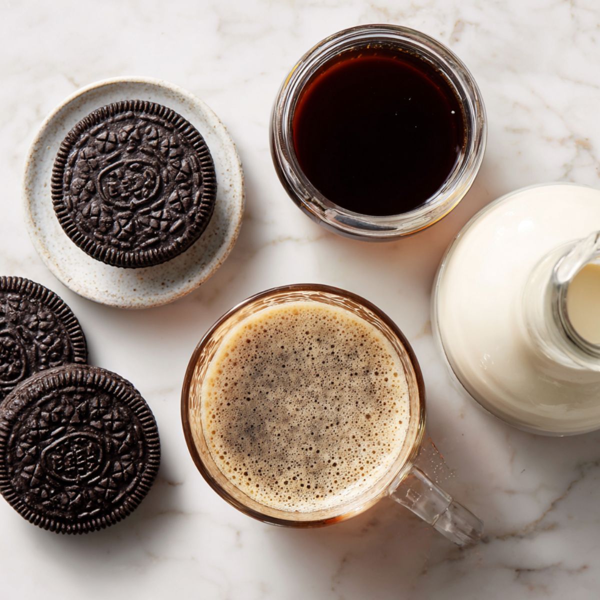 Flat lay of Oreo iced coffee ingredients arranged casually on a white kitchen counter with soft natural lighting.