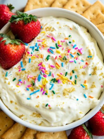 Homemade protein Dunkaroo dip in a bowl with rainbow sprinkles, surrounded by dippers on a white counter