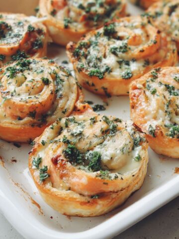 Overhead shot of homemade salmon pinwheels on a white kitchen counter, showing their golden edges and creamy filling.