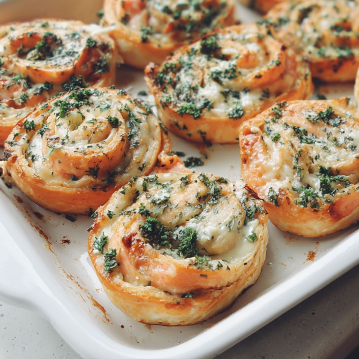 Overhead shot of homemade salmon pinwheels on a white kitchen counter, showing their golden edges and creamy filling.