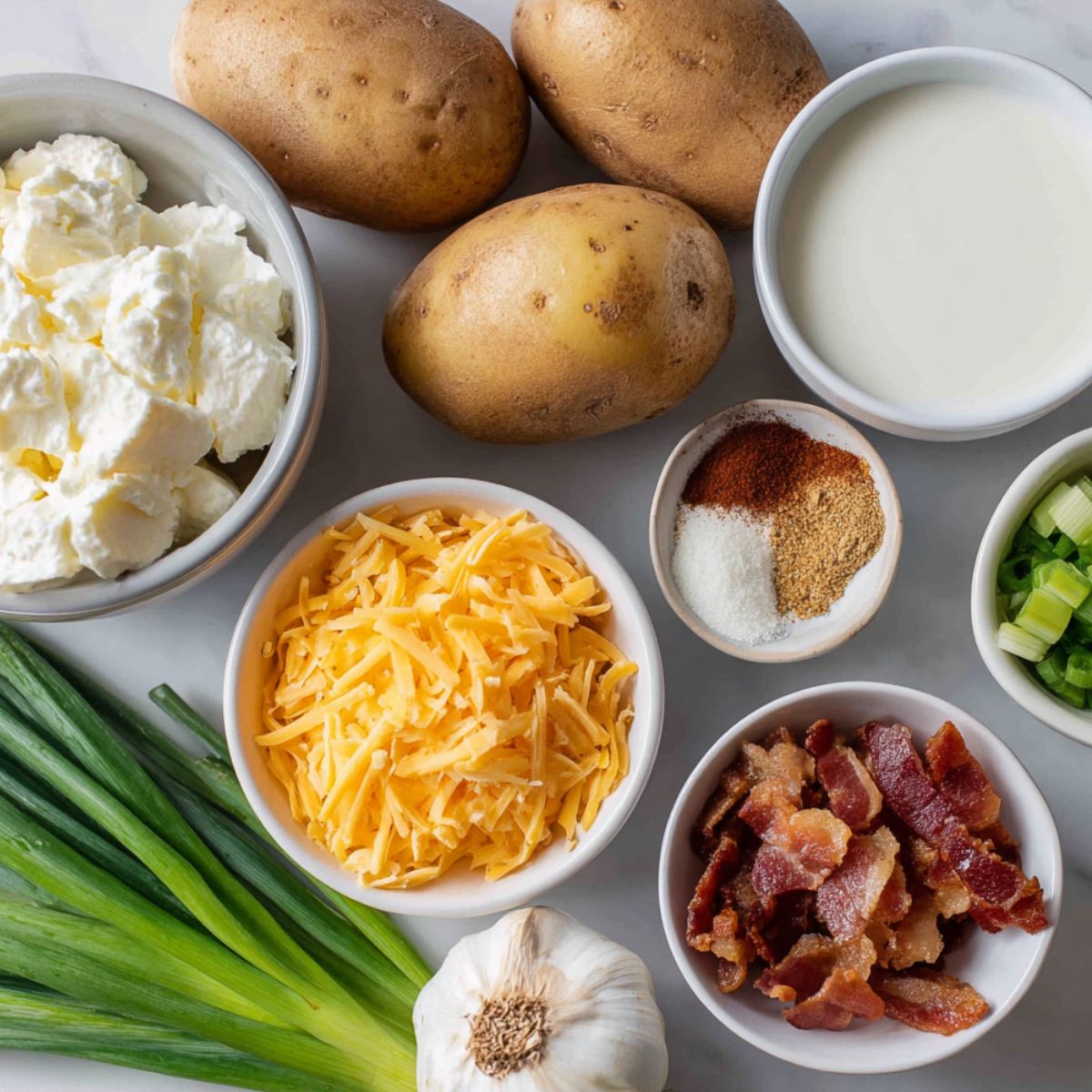 Ingredients for twice baked potato casserole arranged on a kitchen counter, including potatoes, sour cream, butter, milk, bacon, cheddar cheese, and green onions.