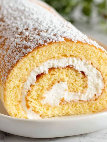 Homemade vanilla swiss roll cake with powdered sugar on a white kitchen counter